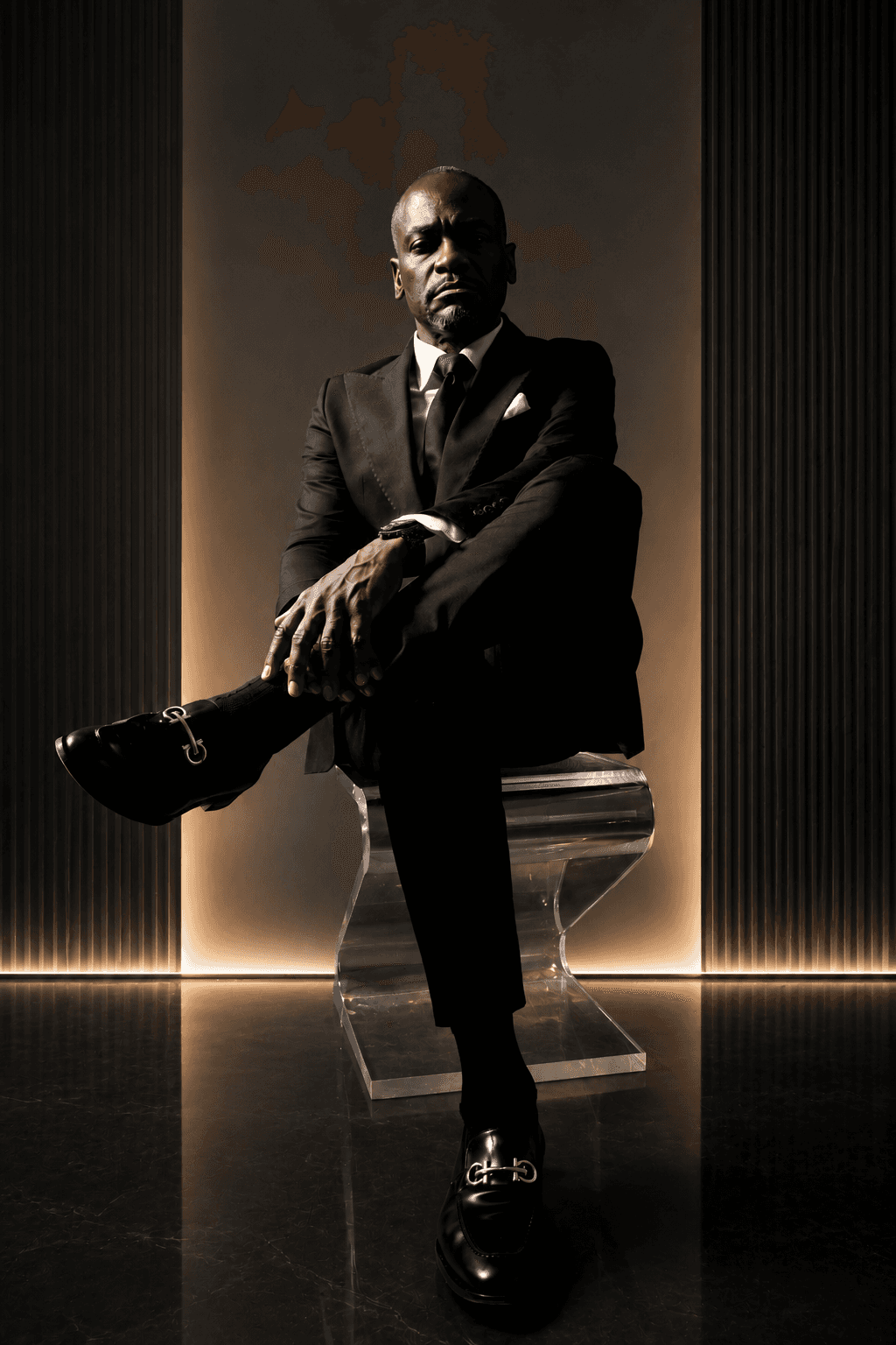 Dr. Glenn Toby seated in a black suit against a warm backlit wall